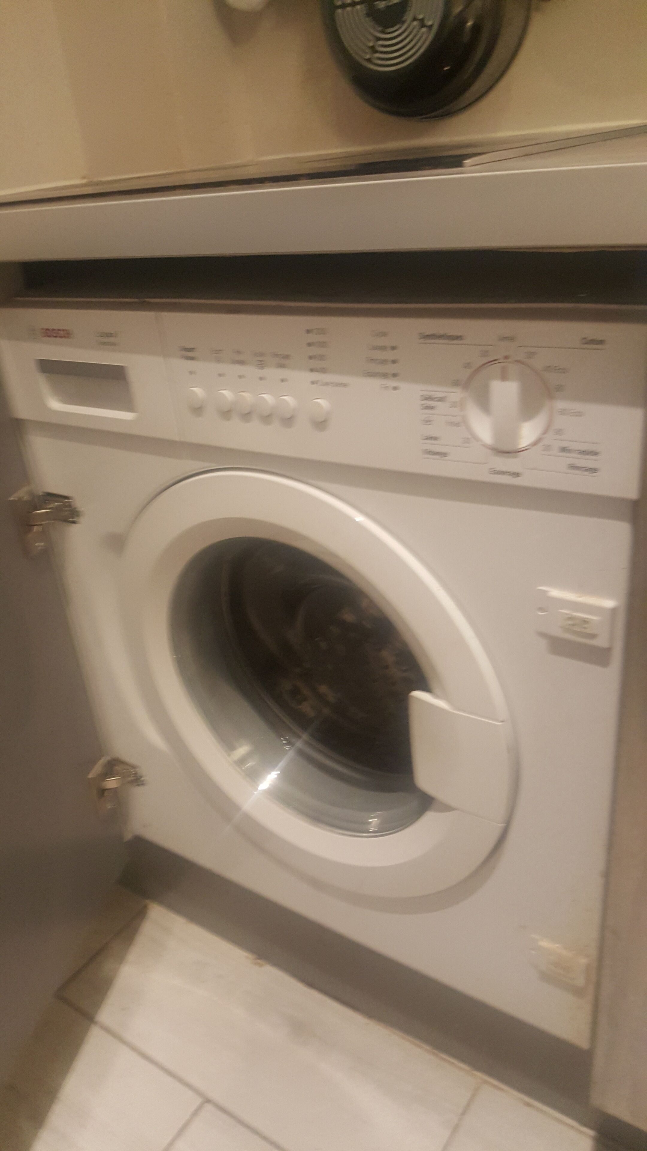 A front-loading washing machine with control panel, door, and control knobs.