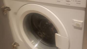 A front-loading washing machine with control panel, door, and control knobs.