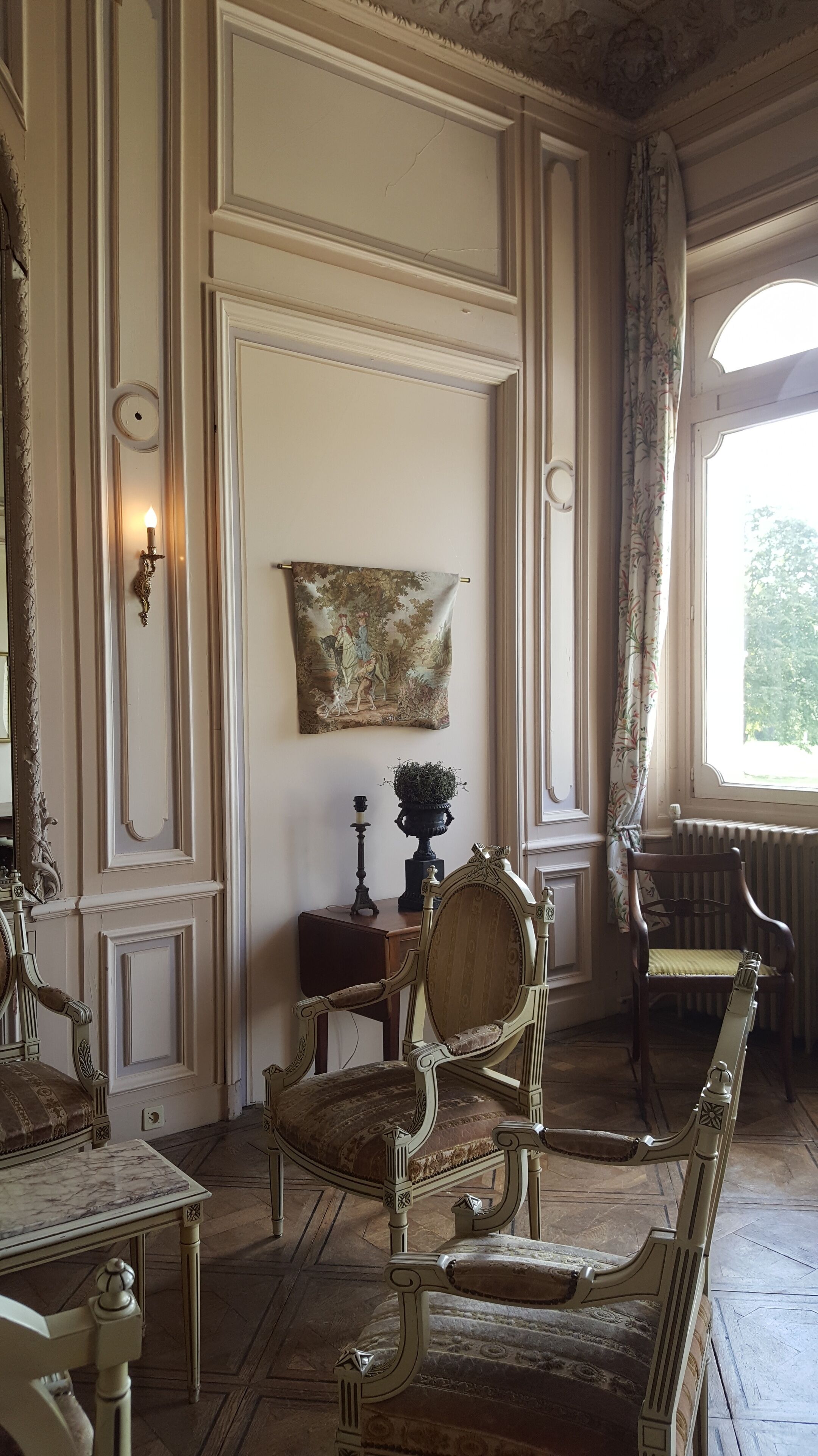 Una habitación con muebles ornamentados, un cuadro en la pared y una ventana con cortinas.