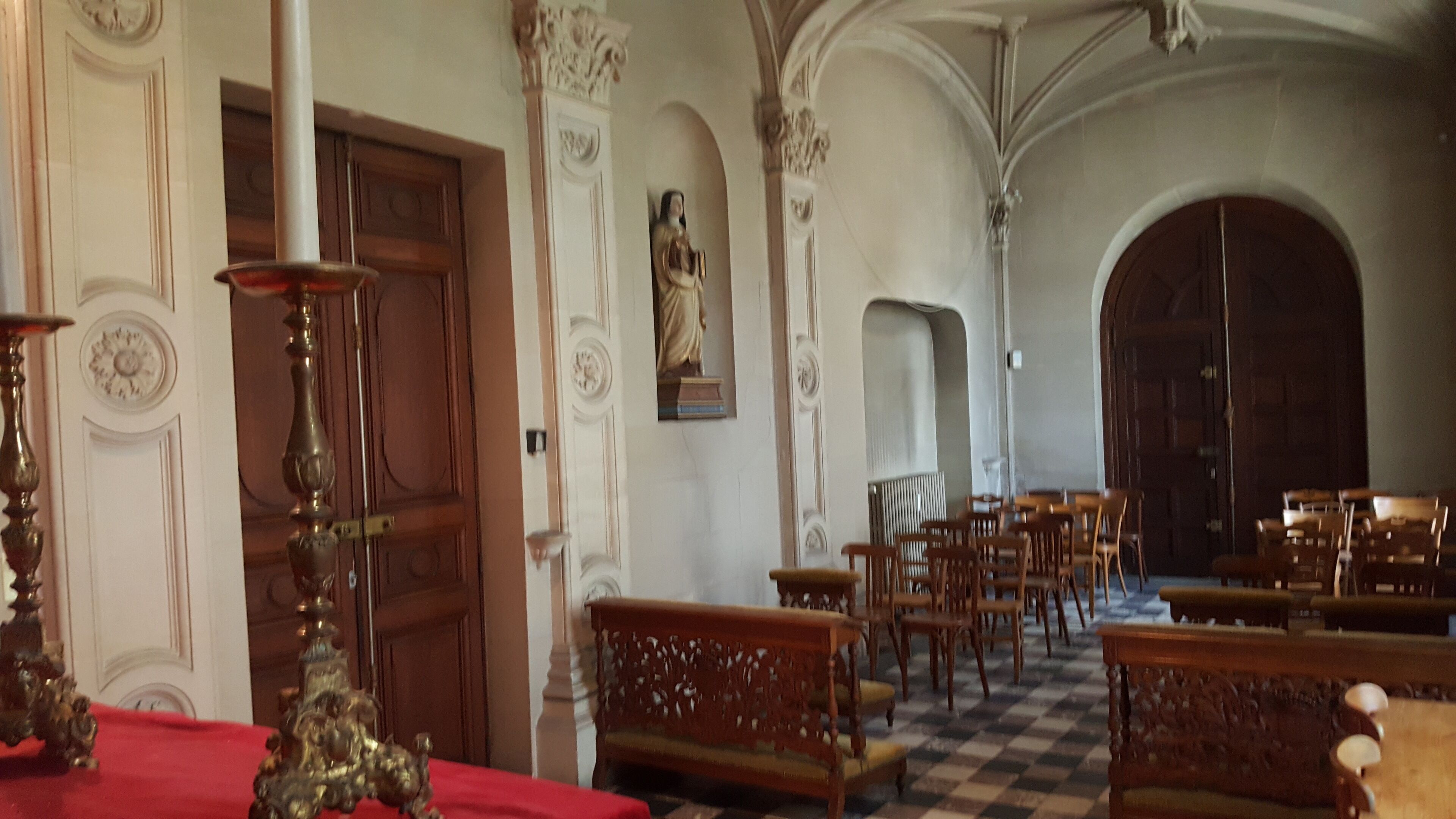 A church interior with wooden pews, a red altar, and a statue.