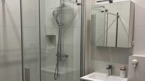 Ett modernt badrum med en duschavdelning med glasväggar, en vit tvättställ och en spegel ovanför tvättstället.