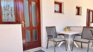 A room with a wooden door, a tiled floor, a small table with chairs, and a window with curtains. - Apartments Fortuna - Studio Apartment (Biograd na Moru)