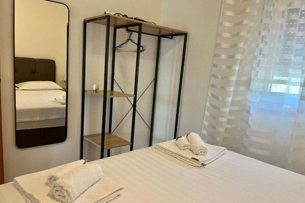 A hotel room with a bed, a mirror, a wardrobe, and a window with sheer curtains.