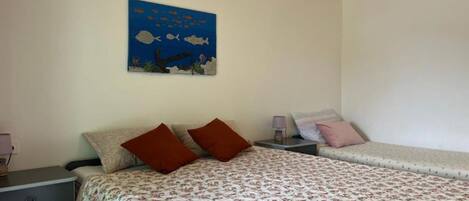 A room with two beds, a nightstand, a lamp, and a wall painting of fish.