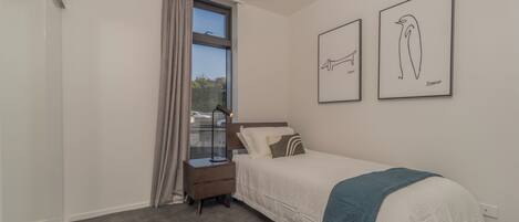 A bedroom with a bed, a nightstand, a window with curtains, and two framed pictures on the wall.