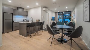 A modern kitchen with a central island, bar stools, and a dining area with a round table and chairs. - High End Centrally located apartment with carpark (Auckland)