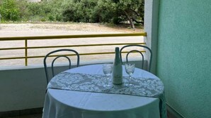 A table with a tablecloth and two chairs, set against a green wall with a view of a road and greenery.