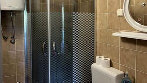 A bathroom with a glass shower enclosure, checkered wall tiles, a toilet with a soap dispenser, and a mirror with a round frame.