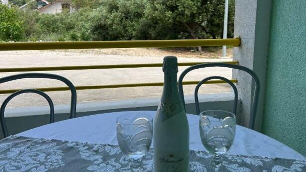 A table with a bottle and two glasses on a balcony overlooking a road and greenery.