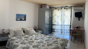 A bedroom with a bed, a nightstand, a dresser, a desk with a chair, and a painting on the wall.