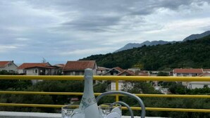 A balcony with a yellow railing overlooking a village with red-roofed houses and a mountain in the background. - One bedroom apartment with balcony-APP4 (Podaca)