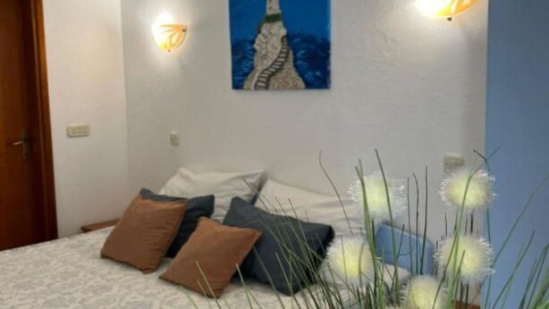 A bedroom with a bed, pillows, a painting, wall sconces, and a door. - One bedroom apartment with balcony-APP4 (Podaca)
