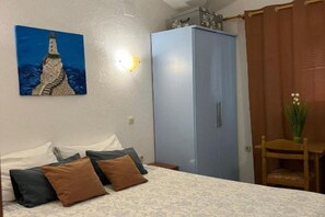 A bedroom with a bed, pillows, a wardrobe, a painting, a nightstand, and a chair.