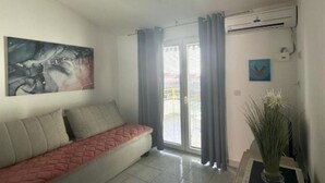 A living room with a sofa, a painting, an air conditioning unit, and a sliding glass door. - Apartments Natali - One Bedroom Apartment with Balcony (APP6) (Podaca)