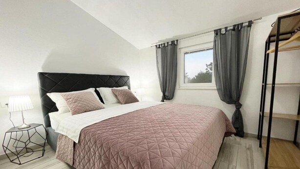 Une chambre à coucher comprenant un lit, une table de chevet, une fenêtre avec des rideaux et une armoire intégrée.