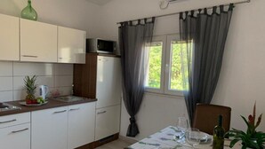 Une cuisine compacte avec des meubles blancs, un four à micro-ondes et un évier. On y trouve une table à manger, mise avec des verres à vin et une bouteille.