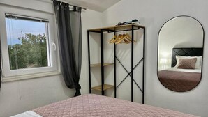 Une chambre à coucher avec un lit, une armoire, un miroir et une fenêtre avec des rideaux.