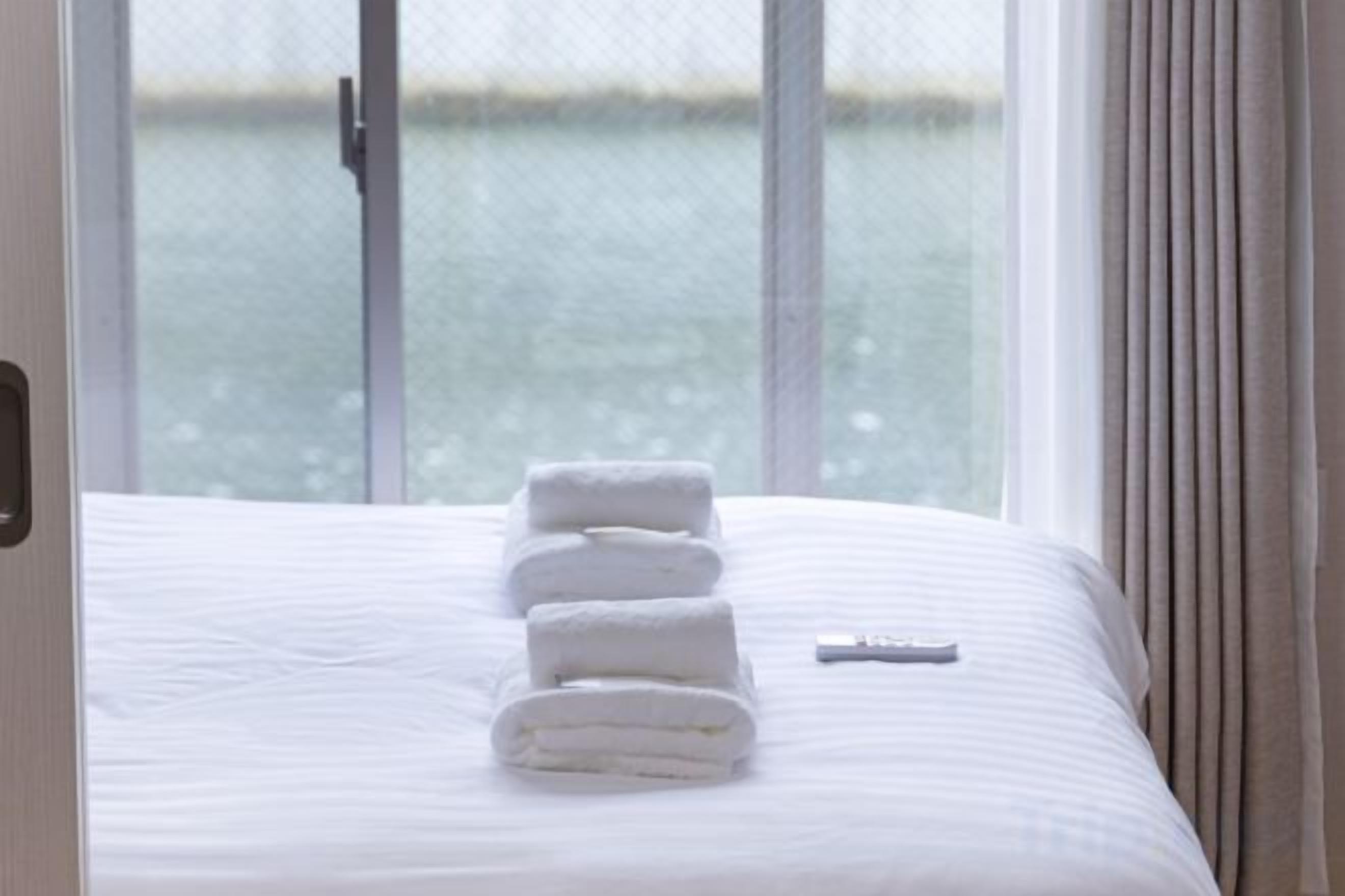 A bed with neatly folded white towels and a remote control on the bed.