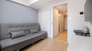 A modern room with a grey sofa, a small table with a kettle, and a door leading to another room. - R Home Sakuragawa Riverside (Osaka)