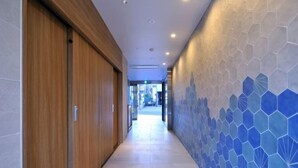 A corridor with wooden doors, a tiled floor, and a wall with a geometric pattern. - R Home Sakuragawa Riverside (Osaka)