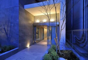 A modern building with a glass entrance, a pathway, and a small tree. - R Home Sakuragawa Riverside (Osaka)