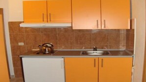 Een kleine keuken met oranje kastjes, een witte koelkast en een waterkoker op het aanrecht.