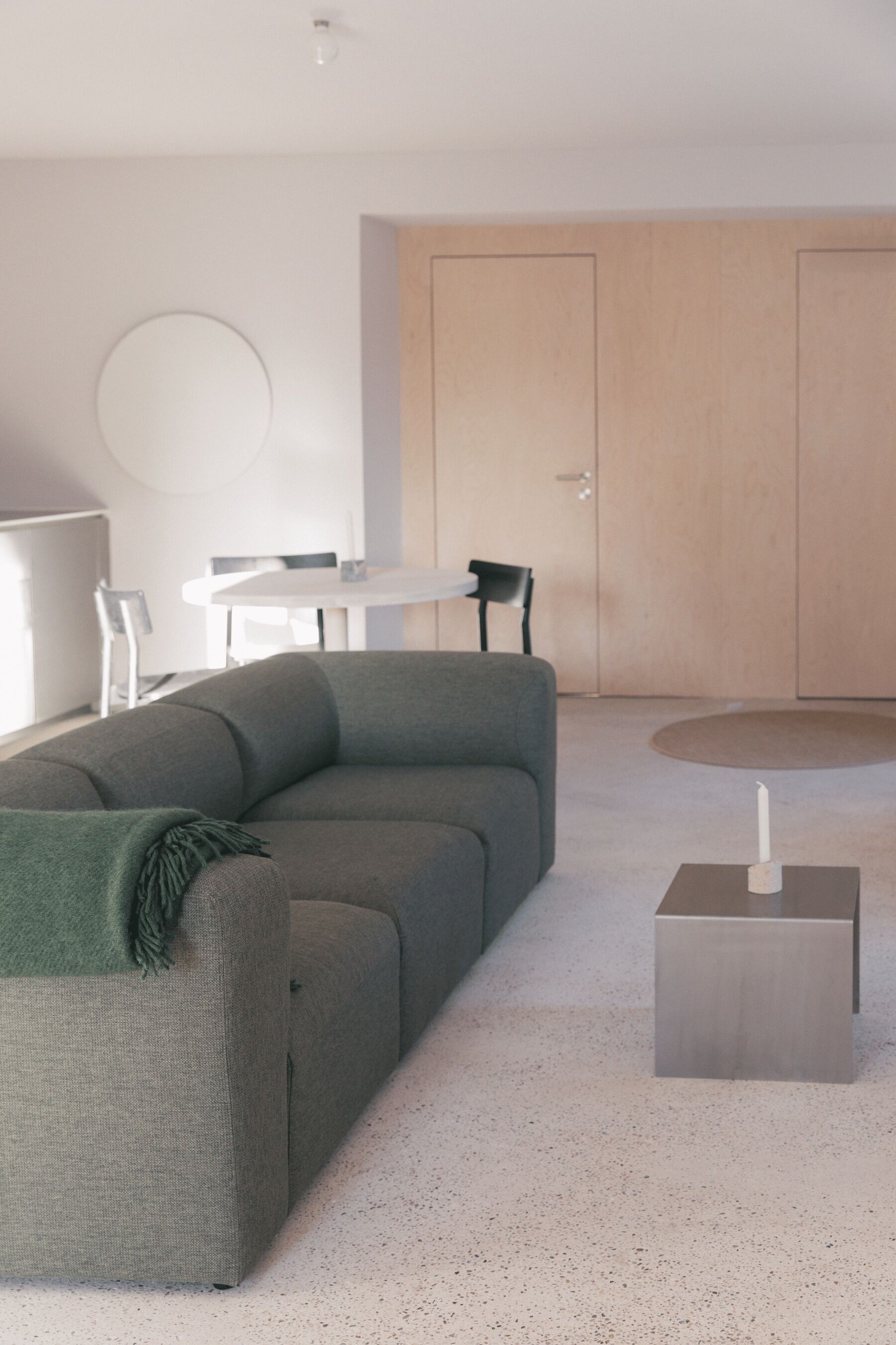 Un salon moderne avec un canapé gris, une petite table sur laquelle est posée une bougie, et une table à manger blanche avec des chaises.