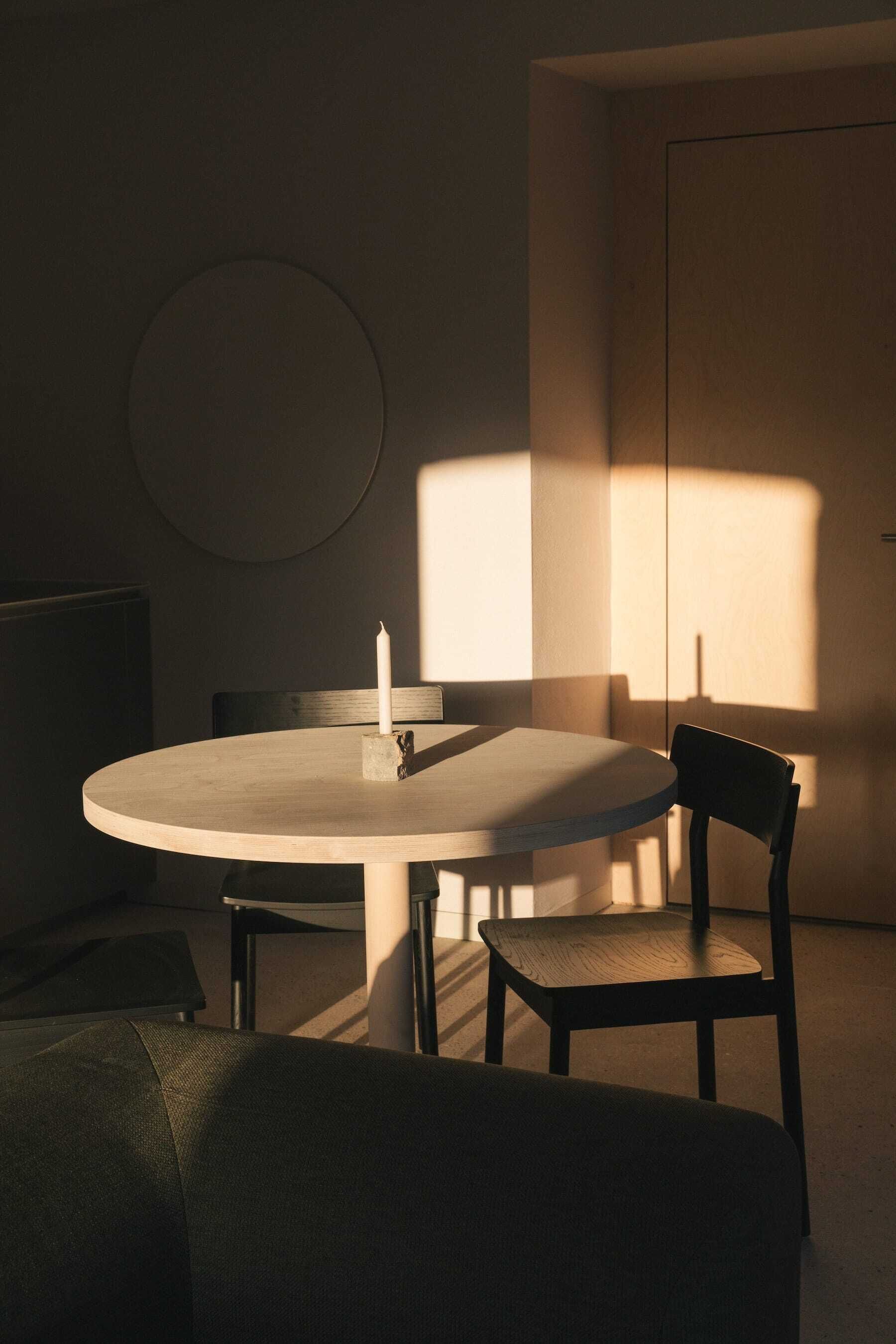A round table with a candle, a chair, and a television in a dimly lit room with a door and a circular wall decoration.