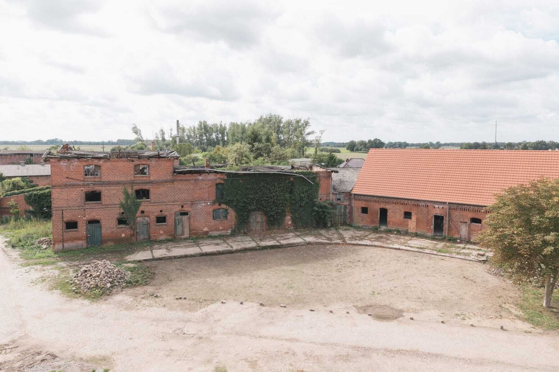 Un grand bâtiment en briques, abandonné, doté de nombreuses fenêtres et d’un toit recouvert de tuiles rouges.