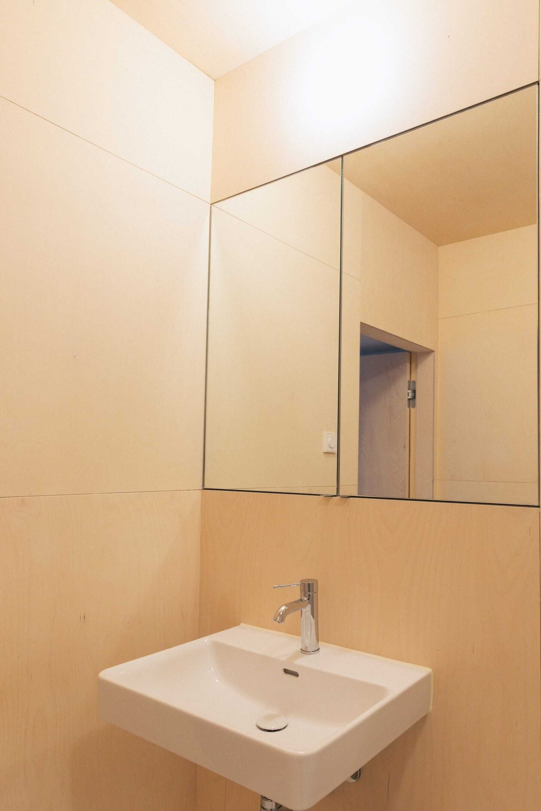 Ein Badezimmer mit weißem Waschbecken, einem Spiegel und Holzwänden.