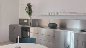 A modern kitchen with stainless steel appliances, a round dining table with two chairs, and a vase with flowers on the counter. - GARDEN FLOOR WEST: Terraces to the south and west (Werben)
