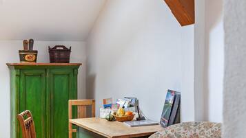 A room with a wooden table, a green cabinet, a chair, and a floral-patterned sofa.