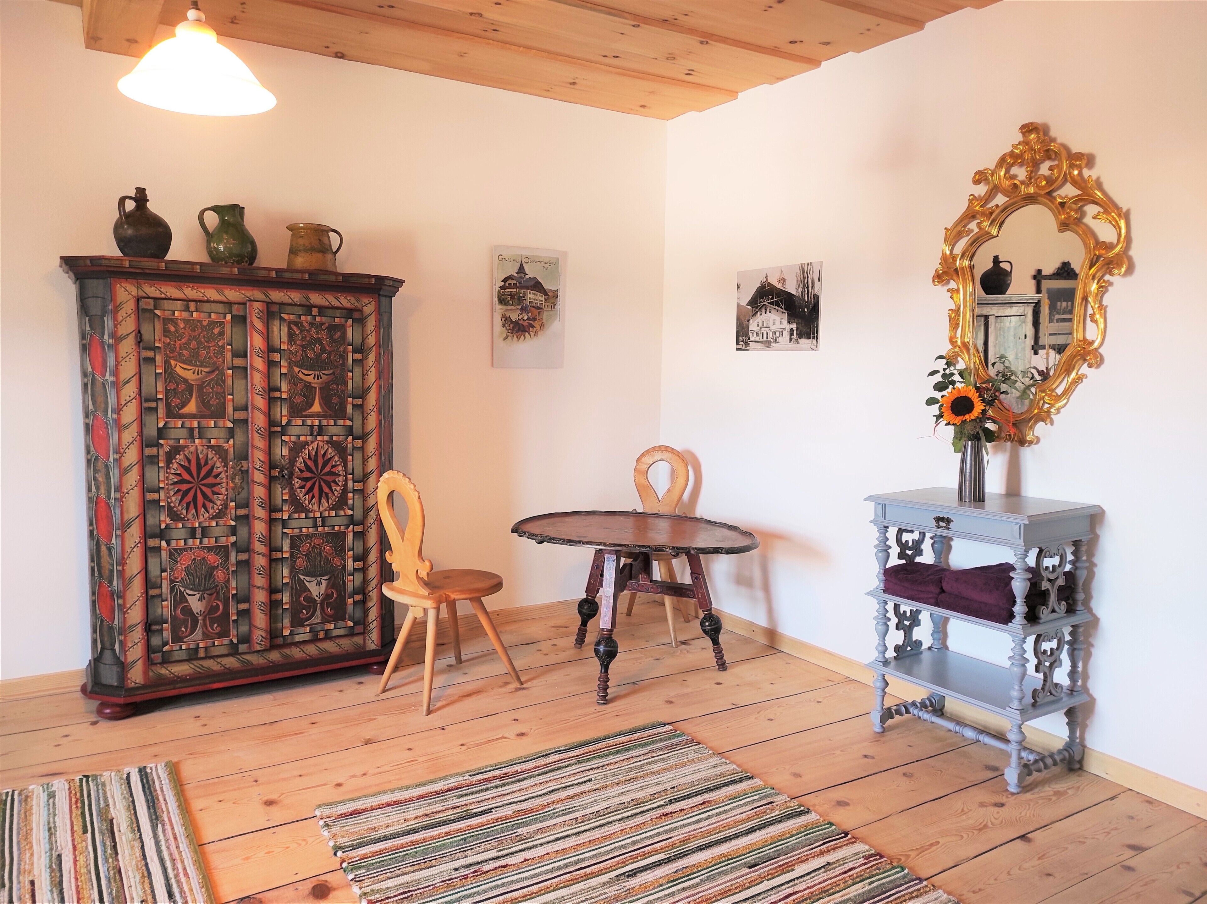 A room with a wooden cabinet, a table, a chair, a mirror, and a rug.