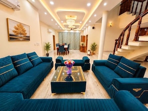 A spacious living area with two large sofas, a coffee table, and a dining area in the background. - Regalia Home (Jammu)