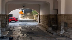 A narrow stone-paved alleyway with a red car parked at the end, leading to a staircase.