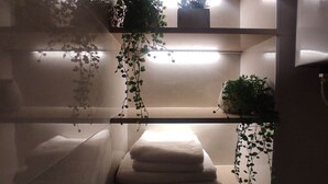 A bathroom with a towel rack, shelves with plants, and a mirror.