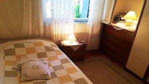A bedroom with a checkered bedspread, a bedside lamp, a nightstand, and a dresser. - Holiday home with parking and 2 rooms (Dubrovnik)
