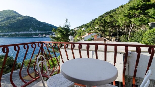 A balcony with a table and chairs overlooking a body of water and a mountainous landscape.