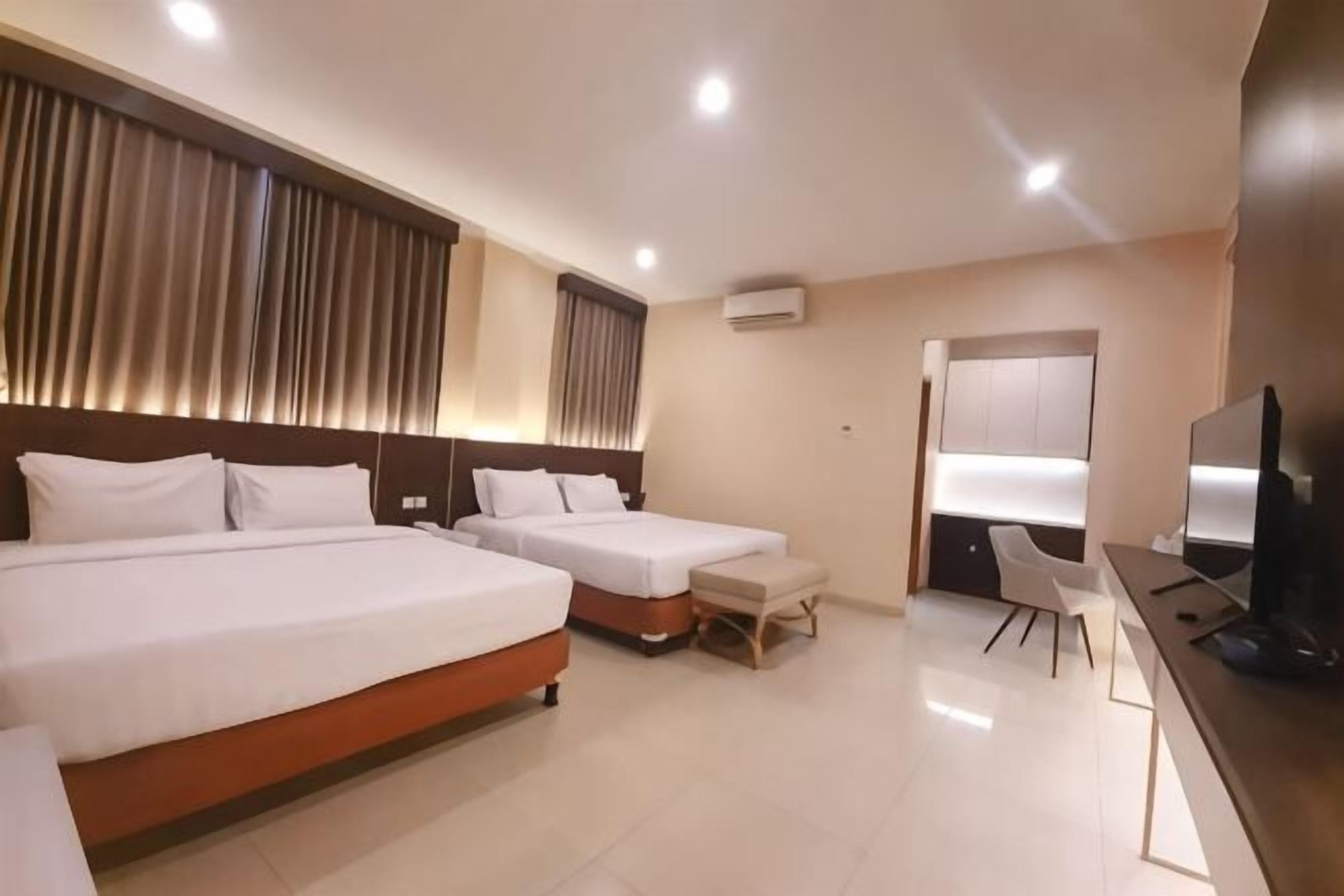 A hotel room with two beds, a desk, a chair, and a television.