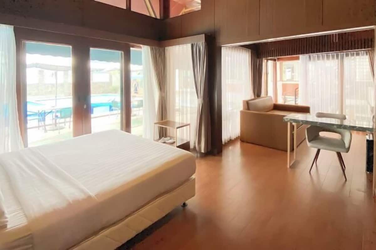 A hotel room with a bed, a seating area with a table, and large windows.