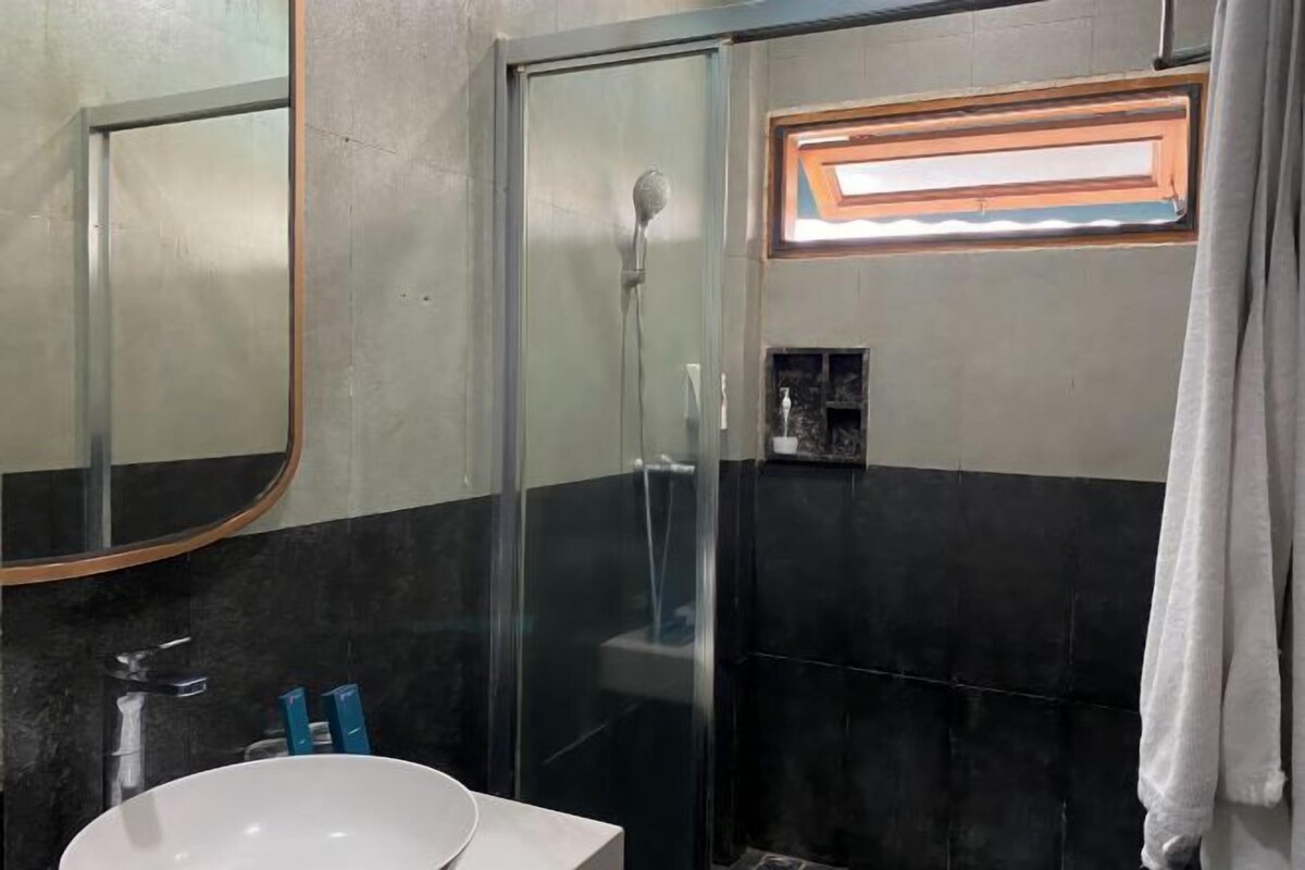 Un baño con cabina de ducha de vidrio, un lavamanos blanco y un espejo.
