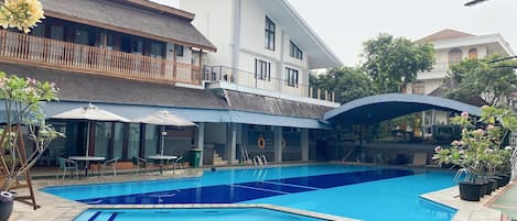 Una piscina con superficie de agua azul cristalina, rodeada por un área de patio techada con mobiliario exterior.