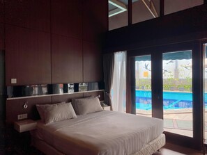 Habitación de hotel con una cama grande, una mesita de noche, un espejo y vista a una piscina al aire libre.