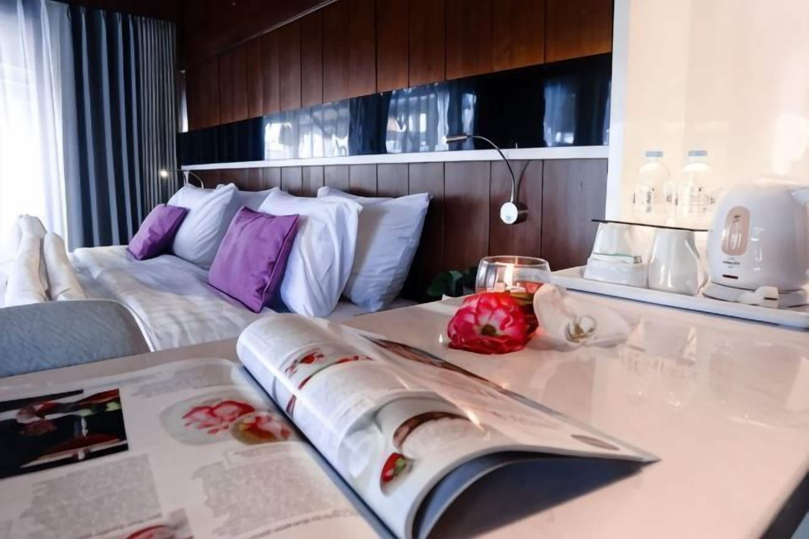 A hotel room with a bed, a table with a magazine, a red flower, and a coffee maker.. Shakti Villa Dago Bandung