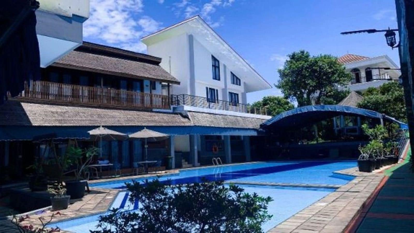 A swimming pool with a covered area, a building with a balcony, and a clear sky.