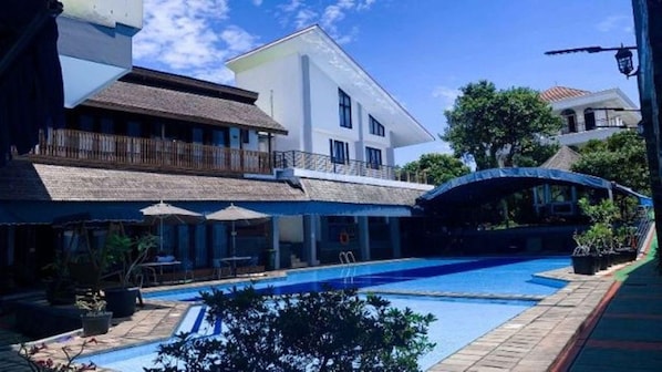 A swimming pool with a covered area, a building with a balcony, and a clear sky.