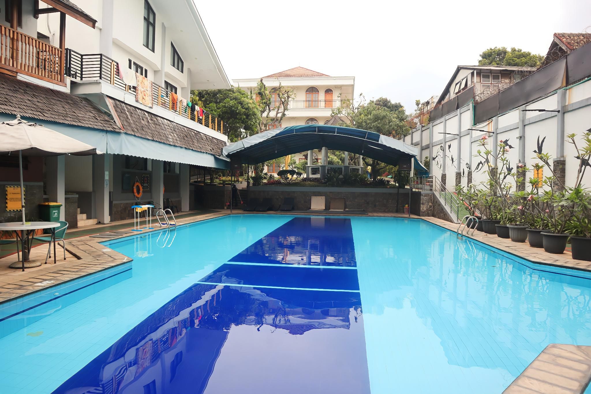 A swimming pool with a clear blue water surface, surrounded by buildings with balconies and outdoor seating areas.