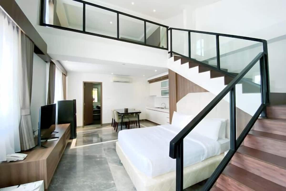 A modern hotel room with a large bed, a desk, a TV, and a staircase leading to an upper level.