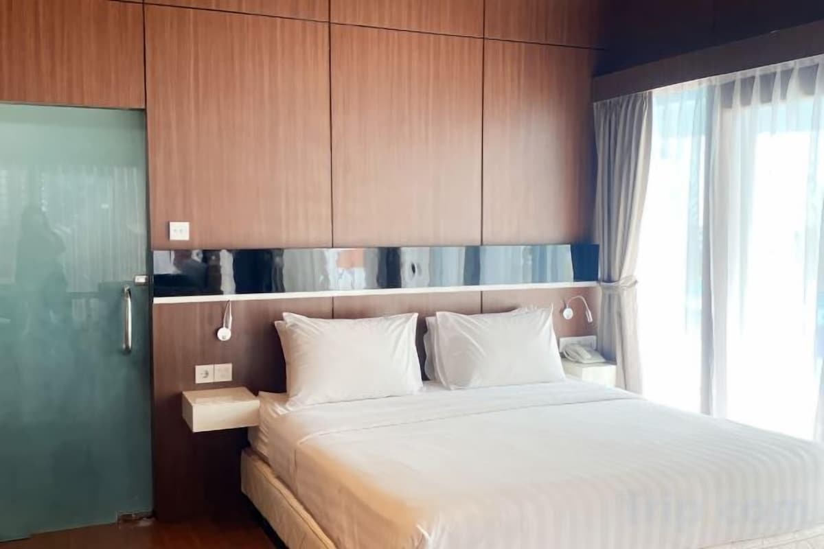 Een hotelkamer met een bed, een houten hoofdeinde, nachtkastje en een raam met gordijnen.