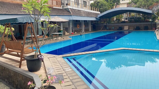 Una piscina con bordeado de baldosas, sillas de descanso y sombrillas.